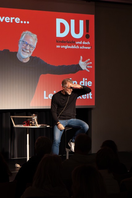 Redner steht auf der Bühne vor der Leinwand