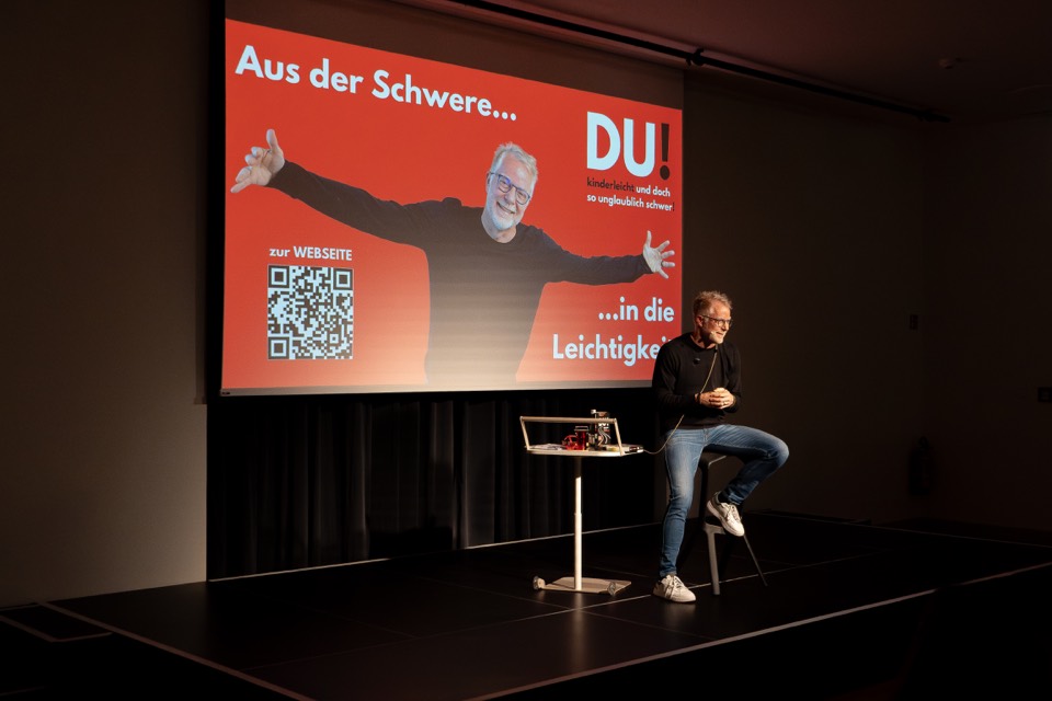 Redner auf der Bühne mit Stehtisch und Leinwand